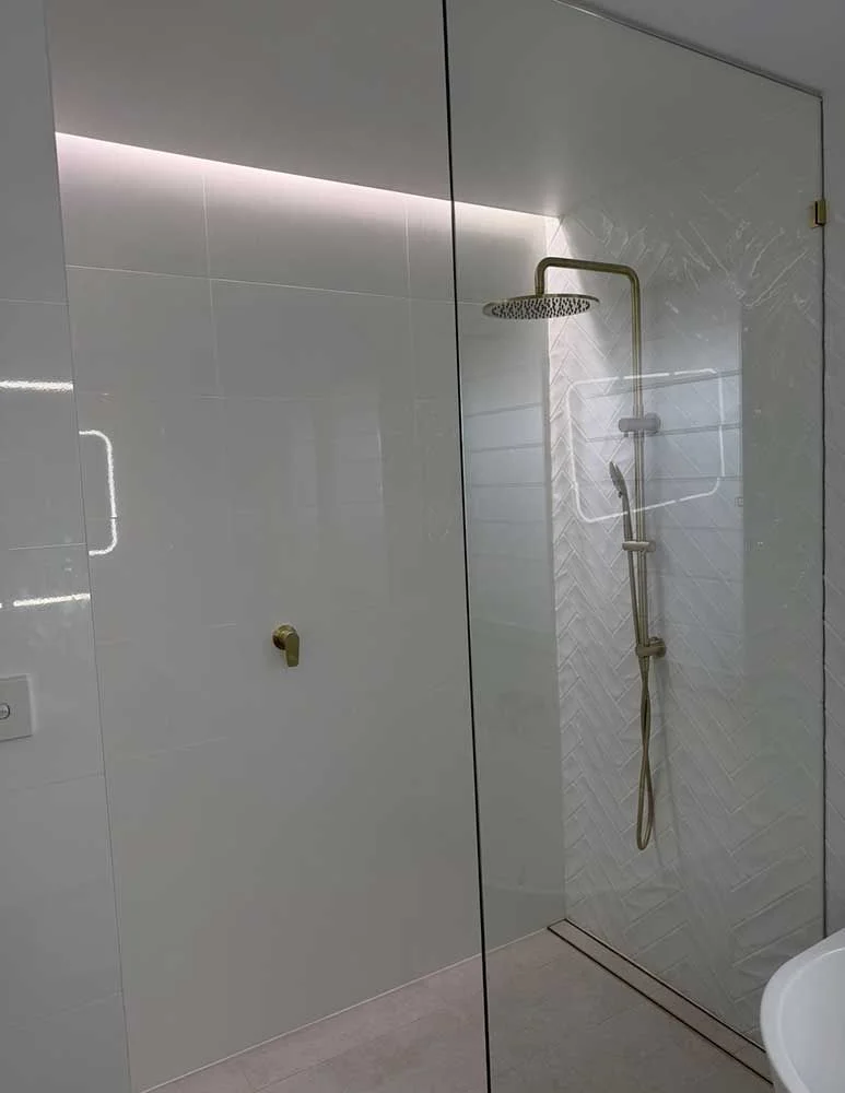 Shower detail showing herringbone tile feature wall, brushed brass rain shower and LED strip lighting by MTS Group