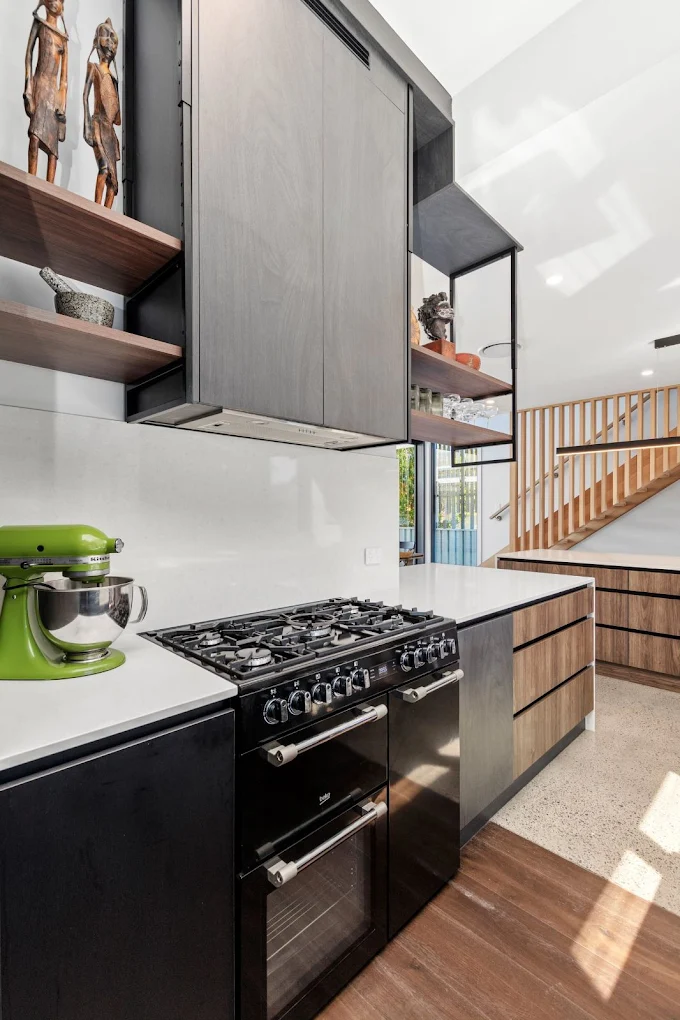 Modern kitchen with freestanding range cooker, timber and black cabinetry, open shelving and polished concrete floor by MTS Group