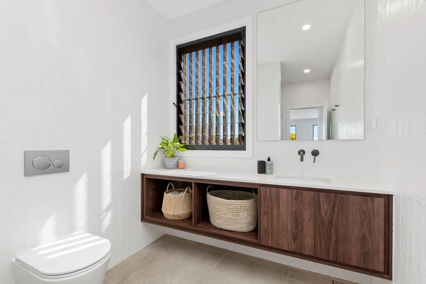 Minimalist bathroom renovation with floating timber vanity, white wall tiles, louvre window and matte black tapware by MTS Group