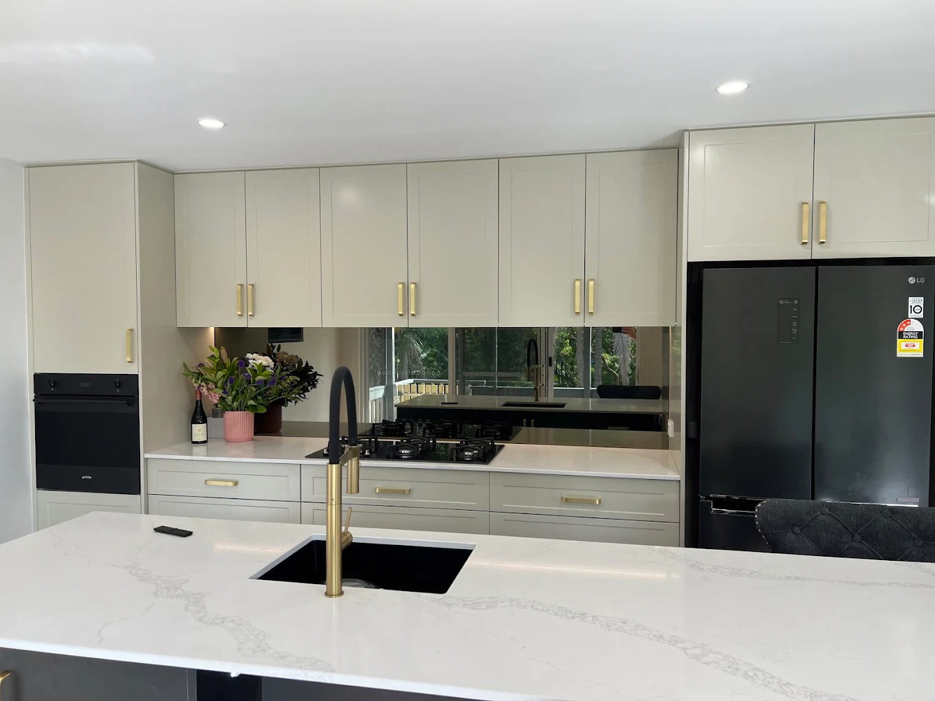 Kitchen detail — shaker cabinetry with mirror splashback, brass tapware and stone benchtop by MTS Group