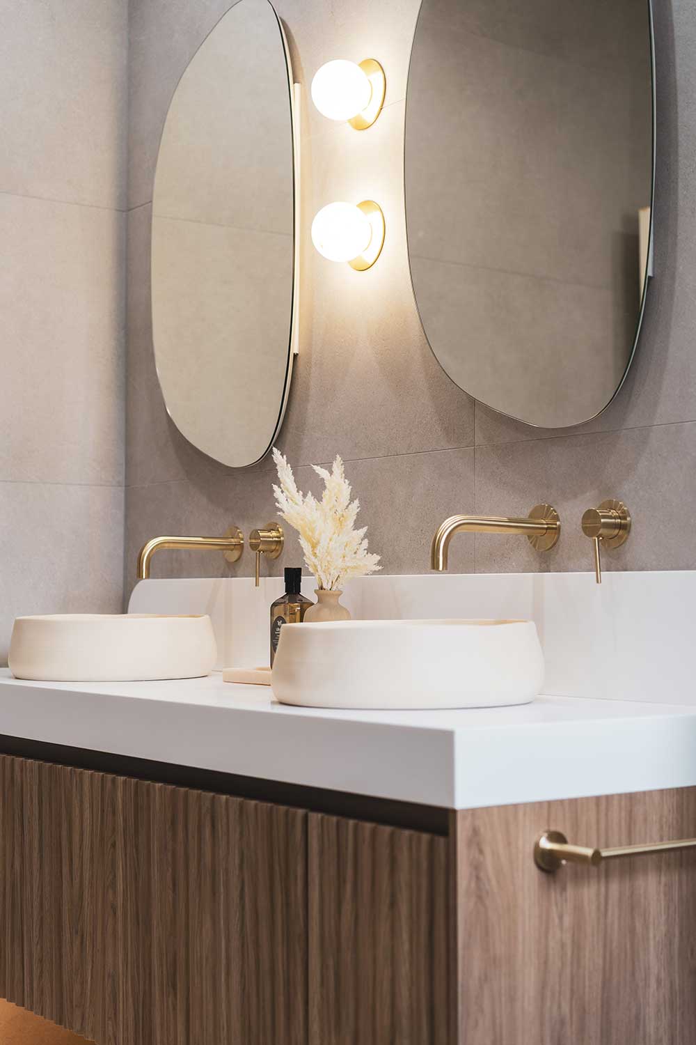 Double vanity bathroom renovation with vessel basins, brass wall-mounted taps, oval mirrors and timber vanity by MTS Group
