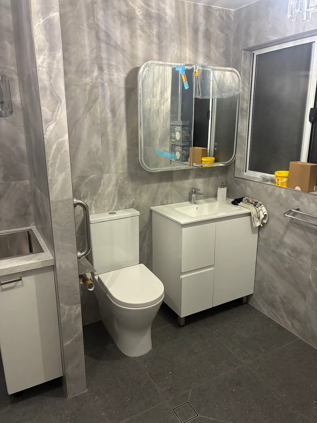 Modern bathroom renovation with grey marble-look wall tiles, white vanity and grab rail by MTS Group
