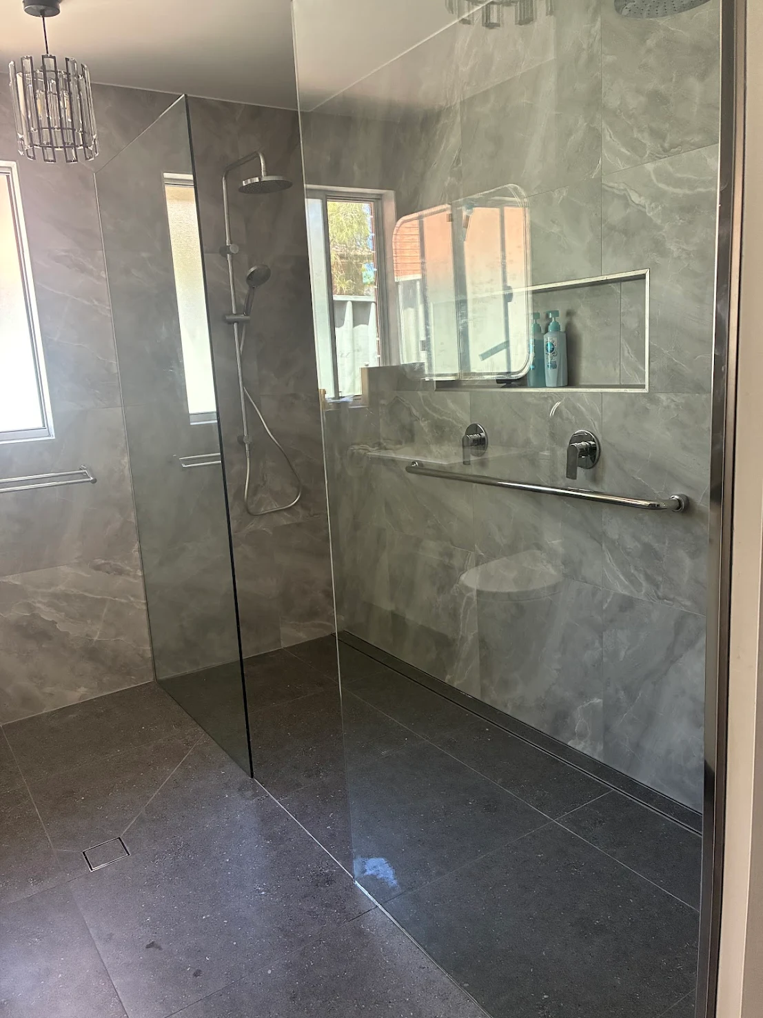 Walk-in shower renovation with grey marble-look tiles, frameless glass screen and recessed storage niche by MTS Group